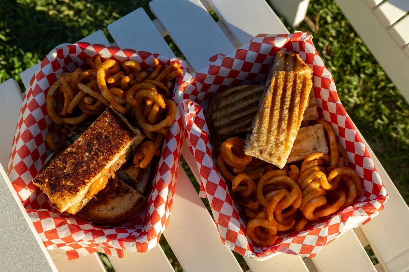 Two baskets of hot-pressed sandwiches and curly fries on a white picnic table